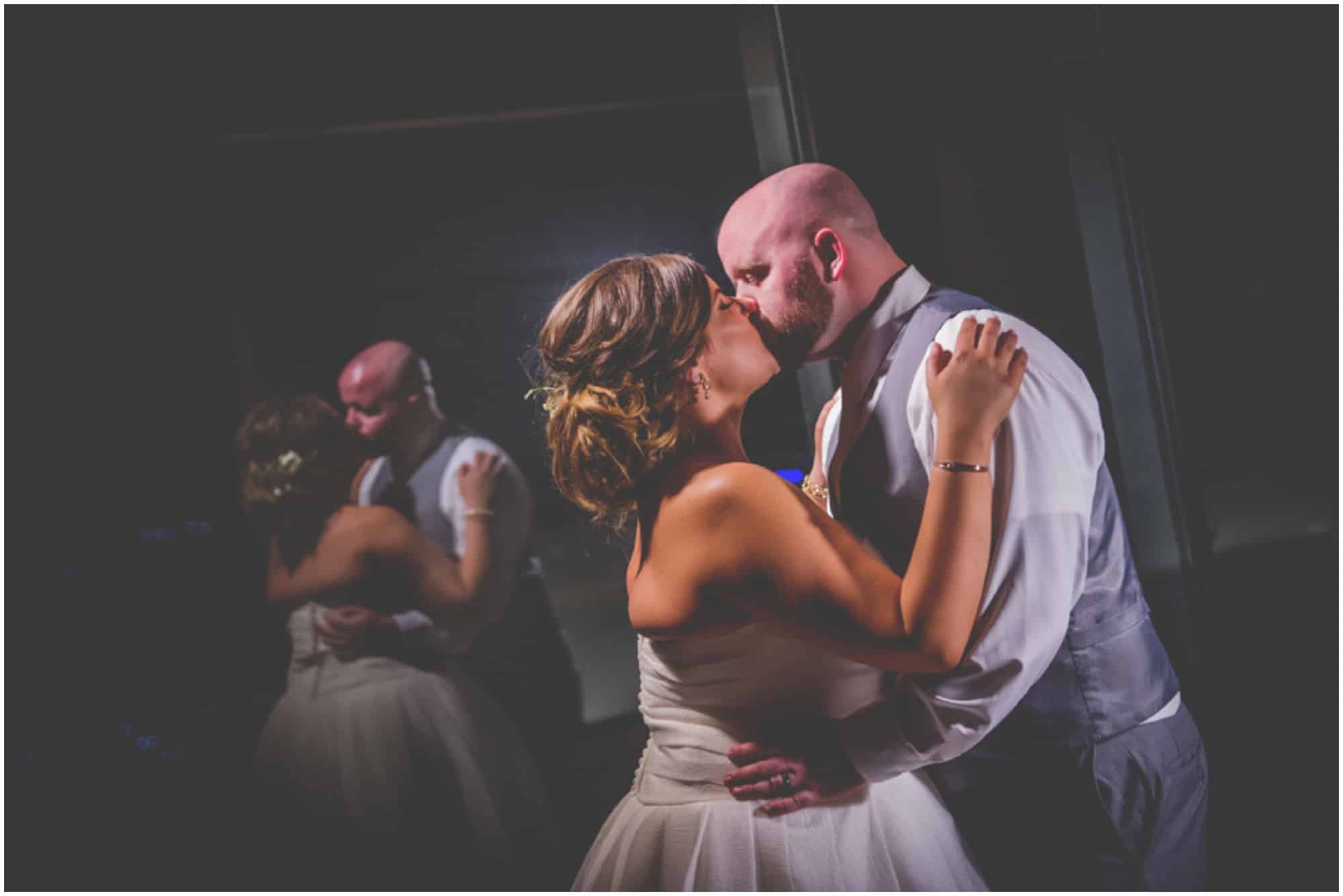 Bride and groom kissing at night with reflection of themselves in window on the balcony outside at Hotel Arista in Naperville